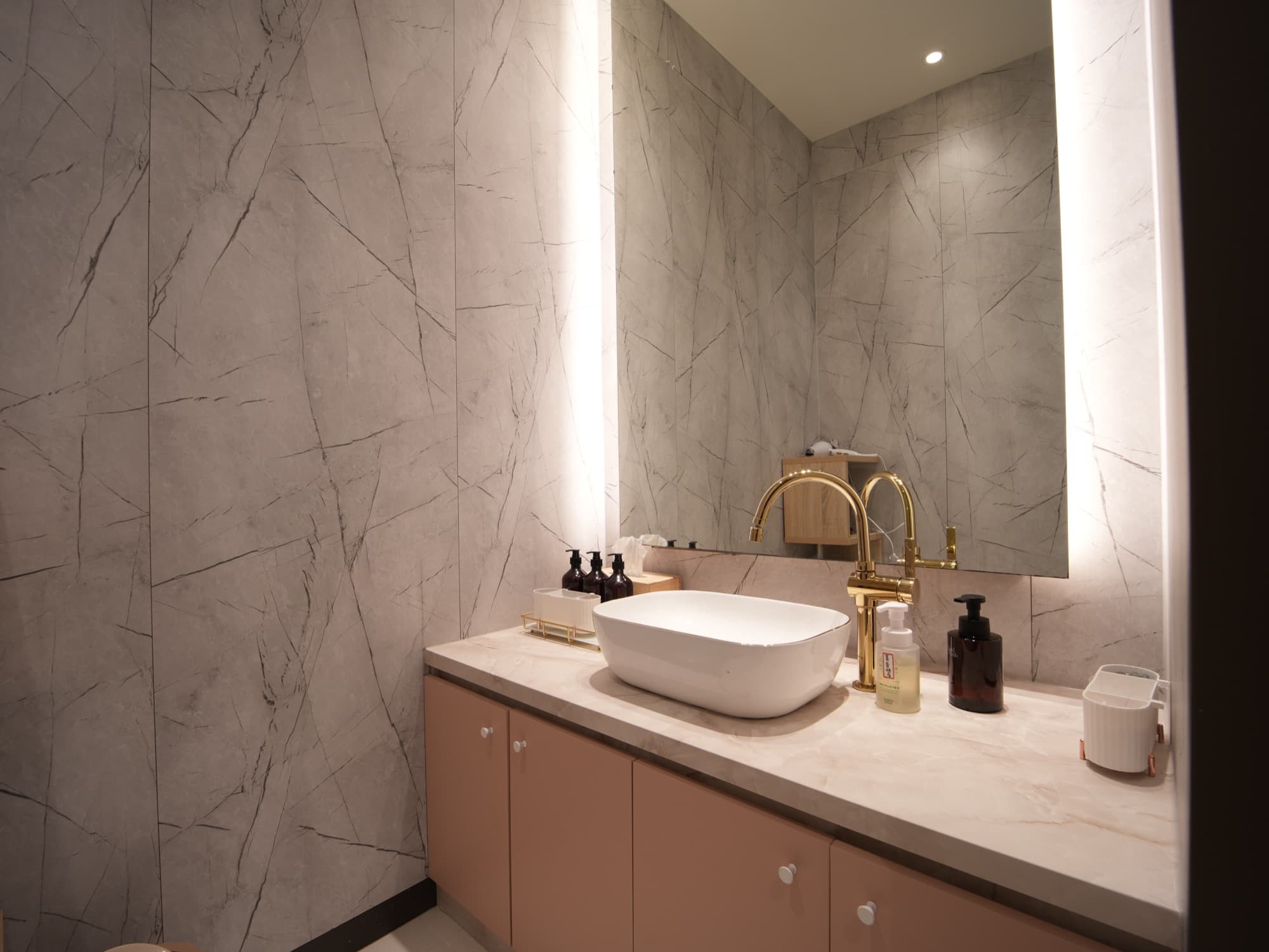 Elegant powder room finished in marble with a vessel basin, gold faucet and backlit mirror