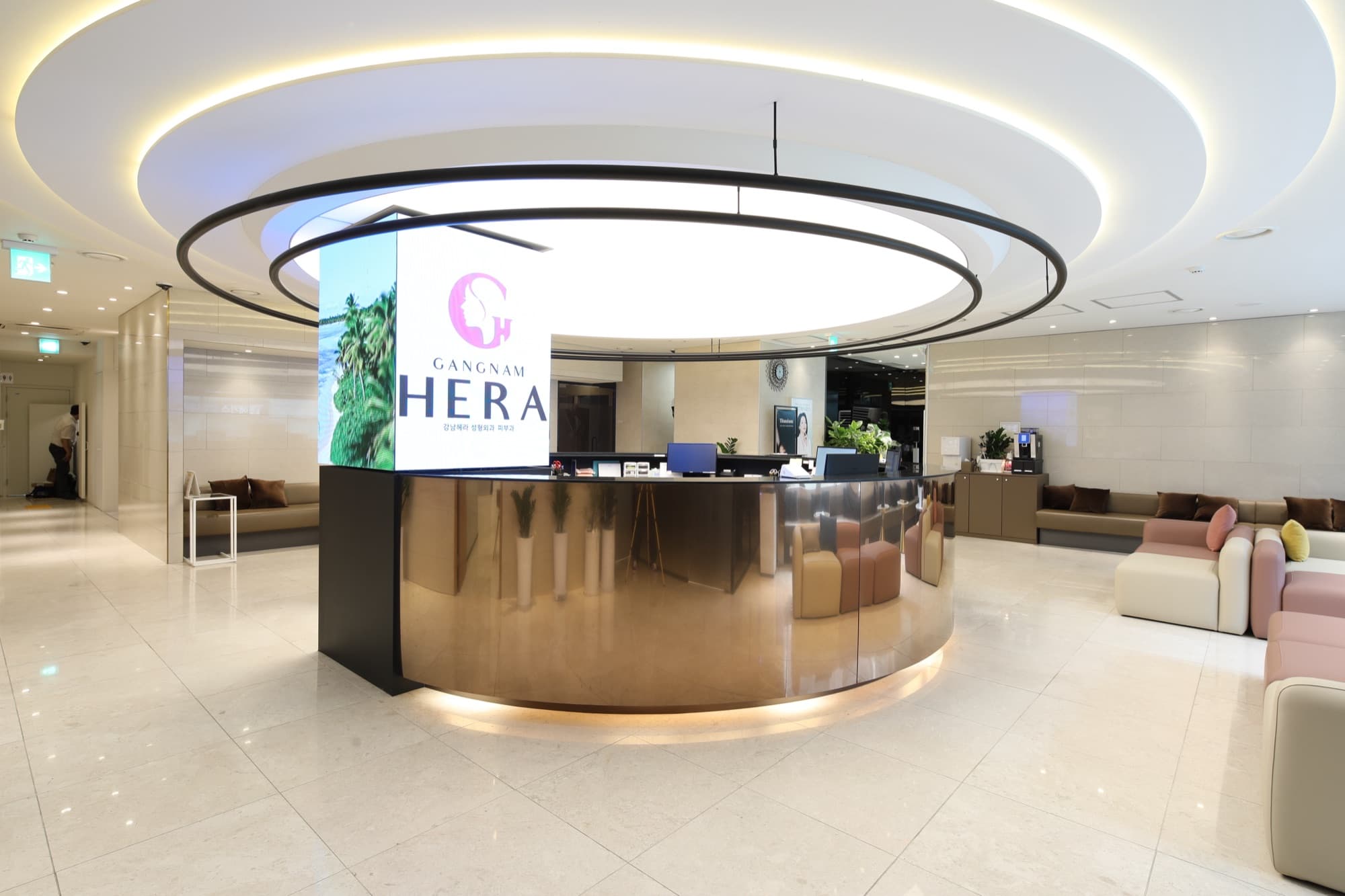 Illuminated GANGNAM HERA brand signage above the polished reception counter, framed by soft lounge seating