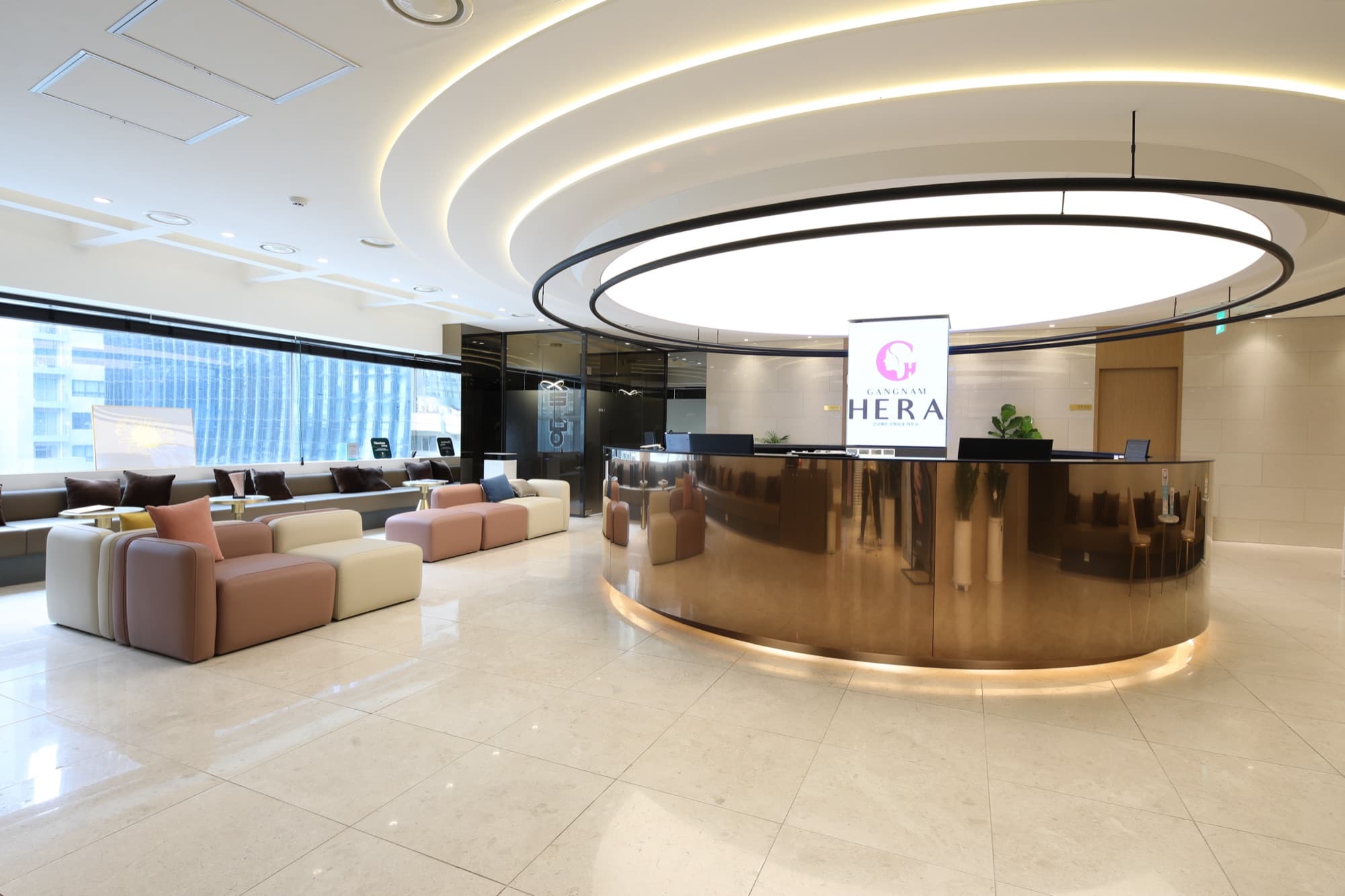 Wide view of the spacious lobby pairing the golden reception island with a warm waiting lounge and city-view windows